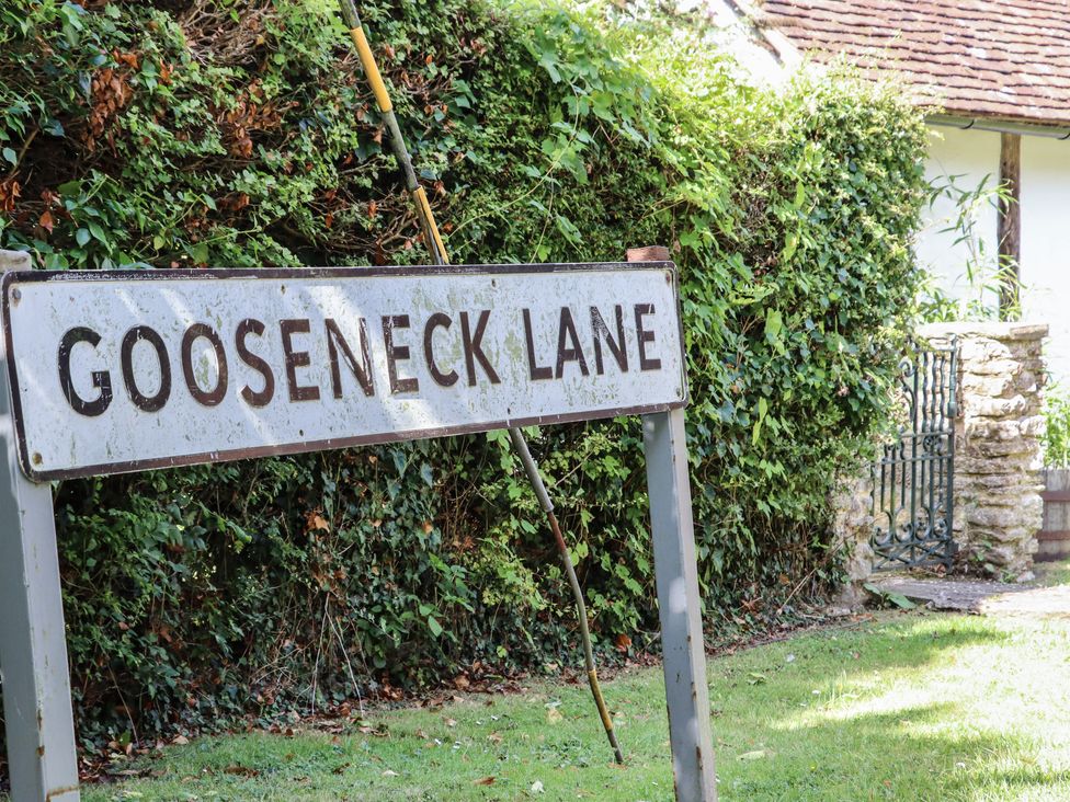 A metal street sign that says Gooseneck Lane next to a hedge and a small gate at The Old Stables in Headcorn