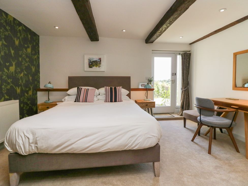 A bedroom with a bed pillows lamps bedside tables a chair desk mirror and door at Birkwray Barn Outgate near Hawkshead