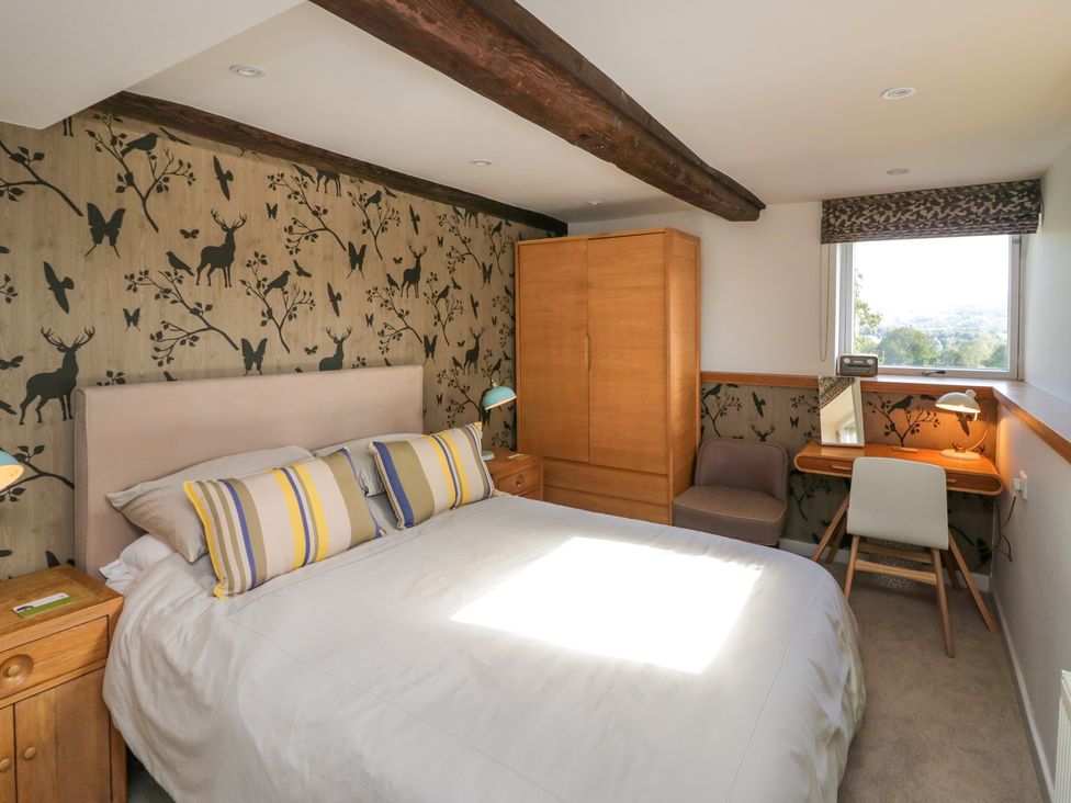 A bedroom with a bed, wooden wardrobe, bedside tables, a chair, and a desk with a lamp at Birkwray Barn in Outgate near Hawkshead