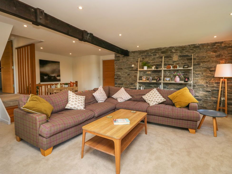 A living room with a large checkered sofa a wooden coffee table and a stone wall at Birkwray Barn Outgate near Hawkshead