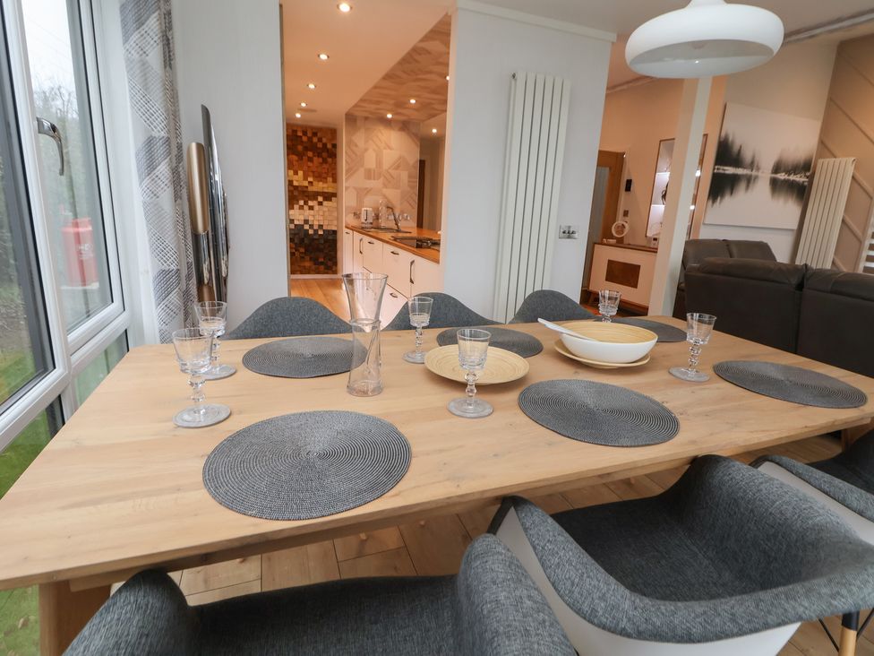 A dining table set with placemats glasses and a bowl in a room with grey chairs and a view into a kitchen and living room at The Lodge @ Racecourse House in Babell near Holywell