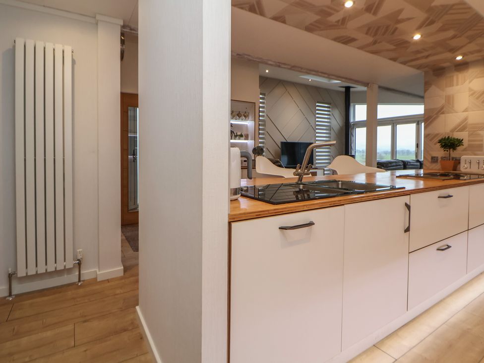 A kitchen with a wooden countertop and white cabinets next to a living area with windows at The Lodge @ Racecourse House in Babell near Holywell