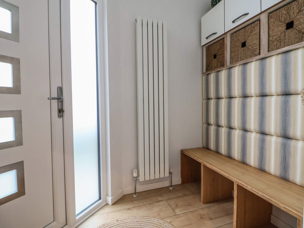 An entrance area with a white door radiator a wooden bench with compartments and storage baskets at The Lodge @ Racecourse House Babell near Holywell