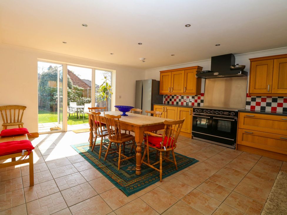 A kitchen with wooden cabinets a dining table and chairs and glass doors leading to a garden at Cedar View in Hainford near Coltishall