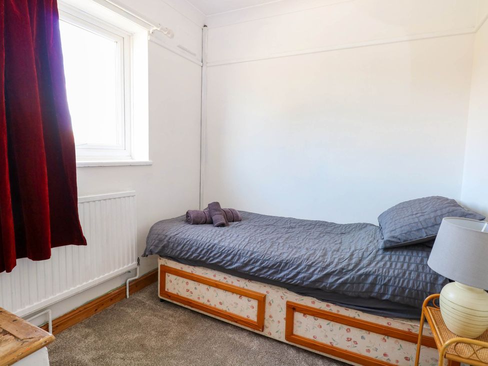 A small bedroom with a single bed covered with gray bedding and towels on top a window with red curtains and a table lamp on a small bedside table at Cedar View in Hainford near Coltishall