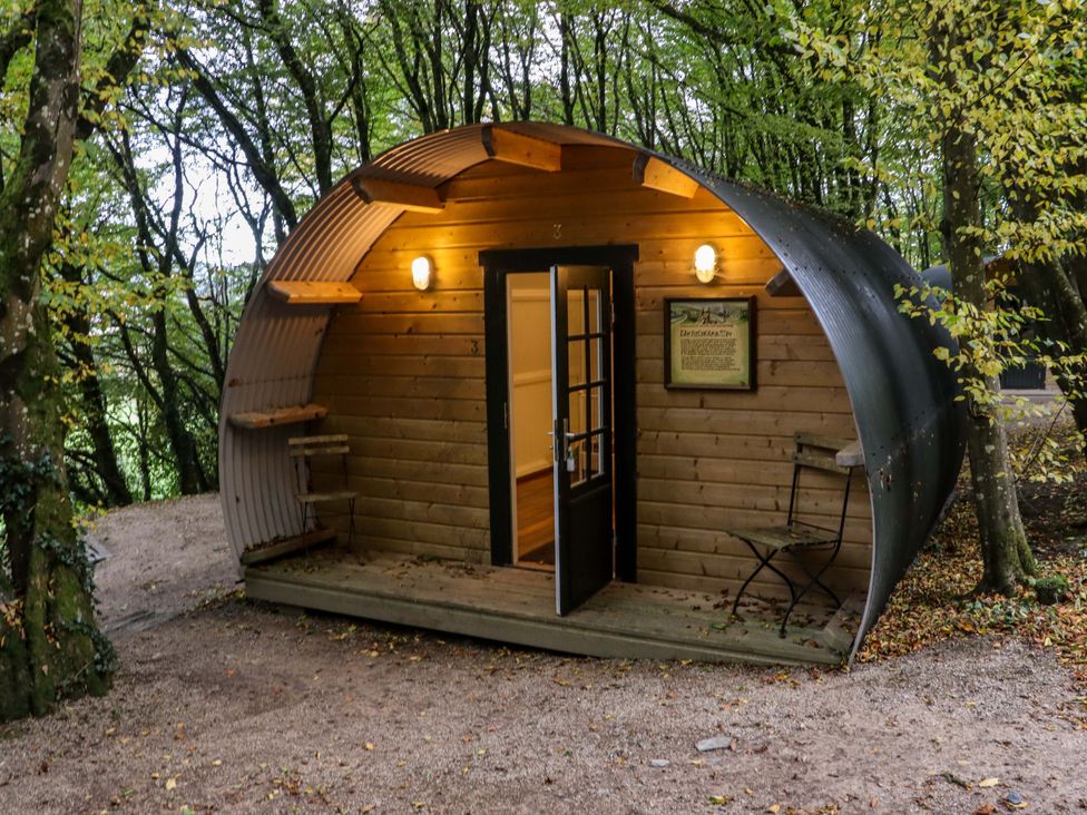 A wooden pod with curved metal roof in a forest with a door open and two metal chairs outside at Ballybeg Pod 7 Ballybeg near Tinahely County Wicklow