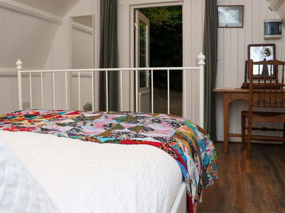 A bedroom with a white metal bed frame with a colorful quilt a wooden desk and chair and an open door leading outside at Ballybeg Pod 7 Ballybeg near Tinahely County Wicklow