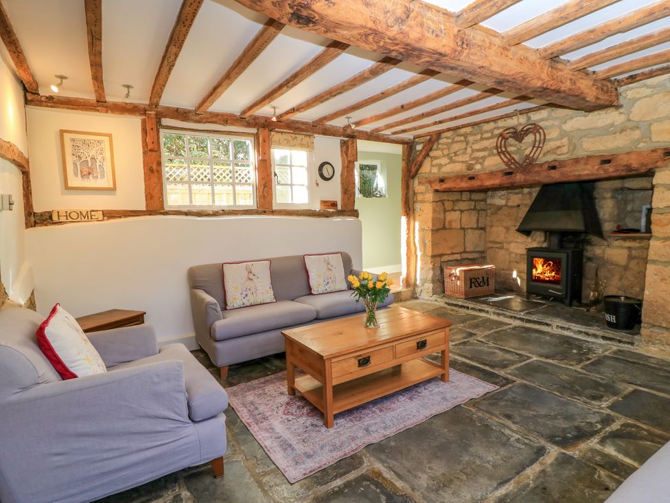 A living room with wooden beams stone fireplace sofas and wooden coffee table at April Cottage in Mickleton Gloucestershire