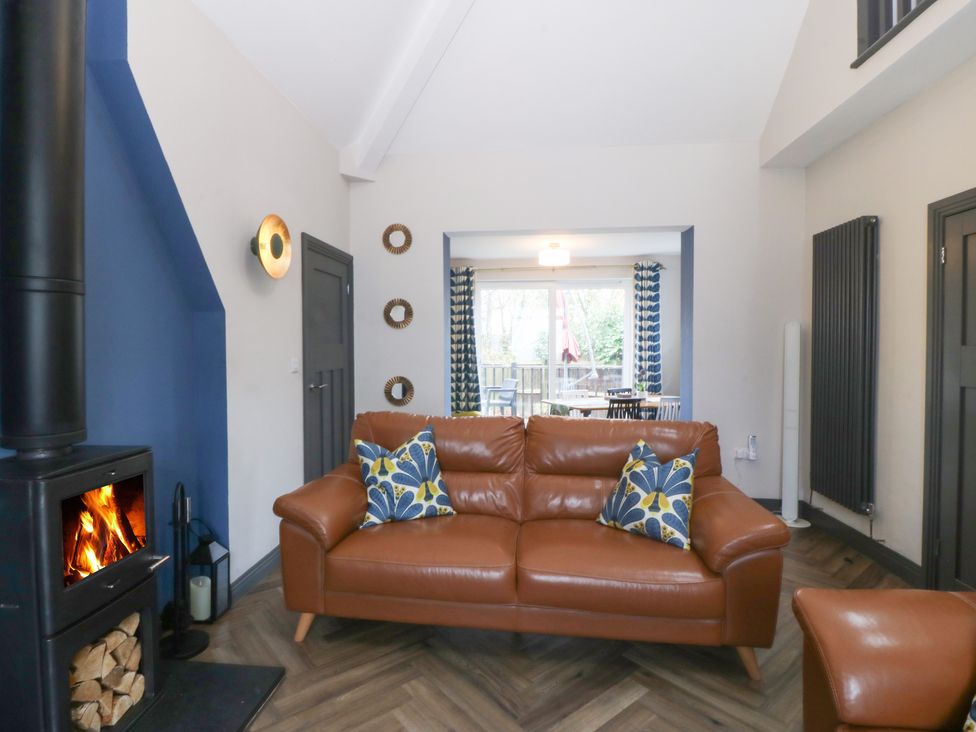 A living room with a brown leather sofa two patterned cushions a black wood stove and a view into a dining area at Trearddur House Cottage in Trearddur Bay