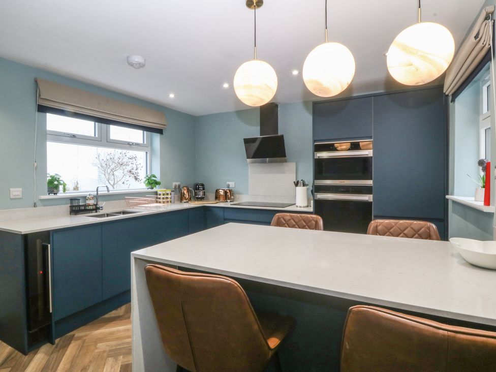 A kitchen with a large island and brown chairs blue cabinets and round pendant lights at Trearddur House Cottage in Trearddur Bay