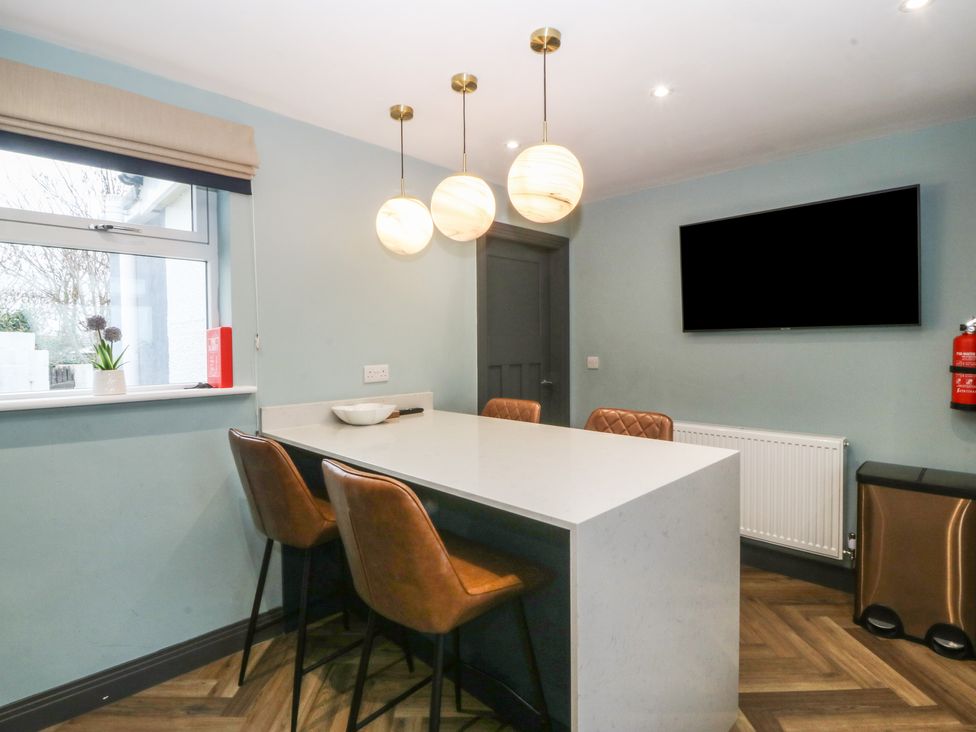 A kitchen with a white island and four brown bar stools under three hanging globe lights at Trearddur House Cottage in Trearddur Bay