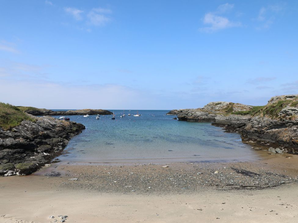 A small sandy beach with rocky edges and boats floating in the water at Trearddur House Cottage in Trearddur Bay