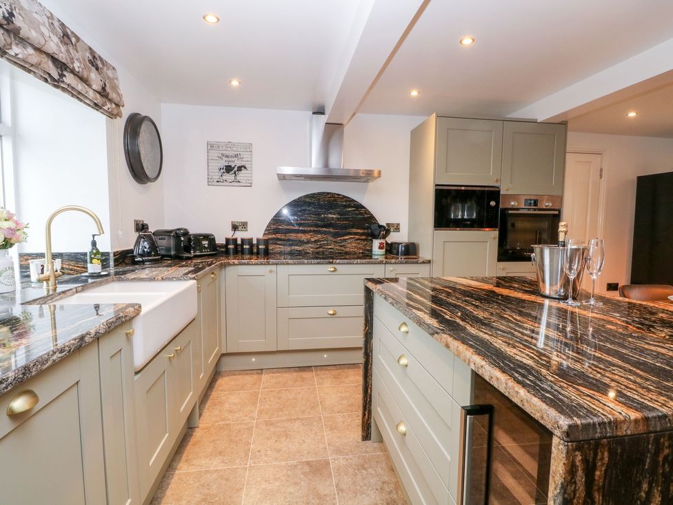 A kitchen with beige cabinets black and brown granite countertops a farmhouse sink and built in ovens at HollyDale Bradnop near Leek