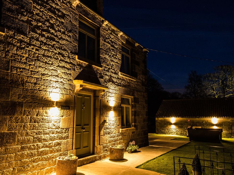 A stone house illuminated by exterior lights at night with a pathway and a small garden at HollyDale in Bradnop near Leek