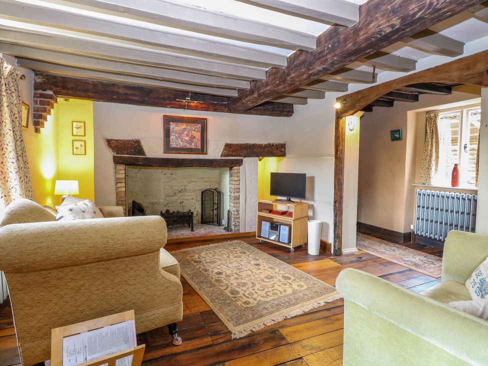 A living room with wooden beams and a fireplace with a TV on a stand at Thatch Cottage in Trunch