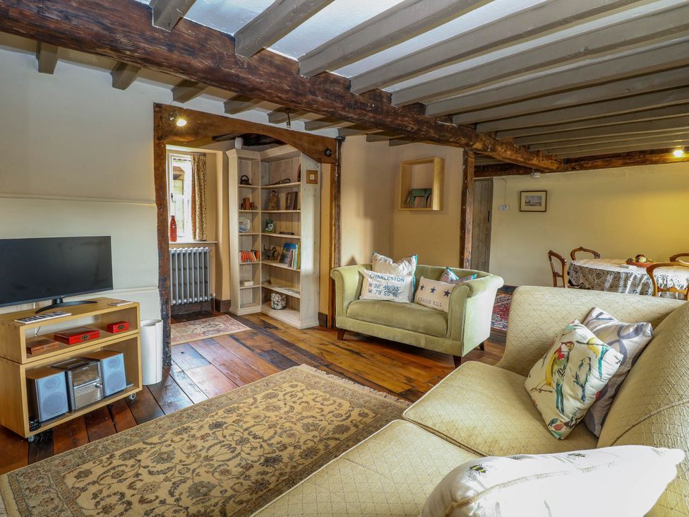 A living room with sofas pillows a television on a wooden stand and a bookshelf at Thatch Cottage in Trunch