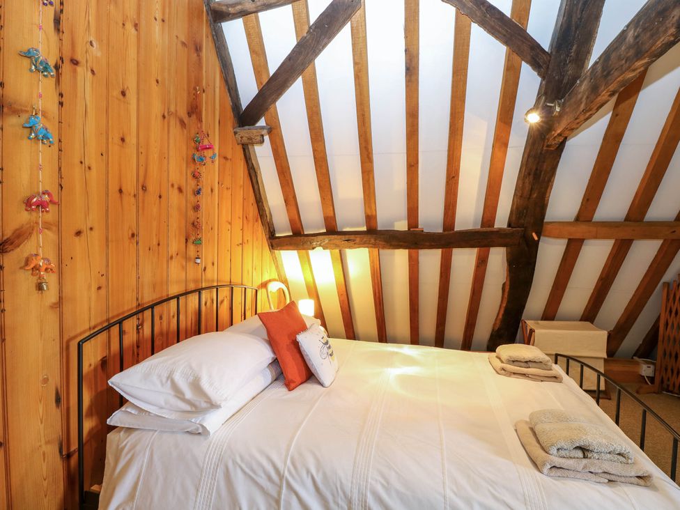 A bed with white linens and pillows in a bedroom with wooden walls and exposed ceiling beams at Thatch Cottage in Trunch