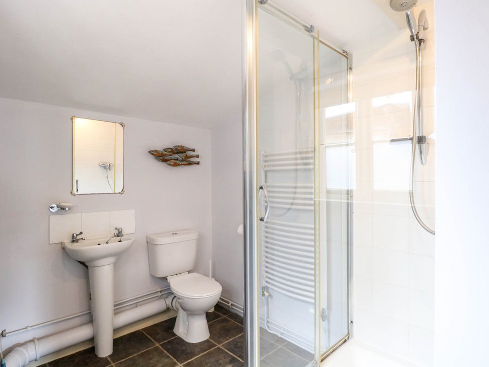 A bathroom with a sink toilet mirror shower and decorative fish wall art at Thatch Cottage in Trunch