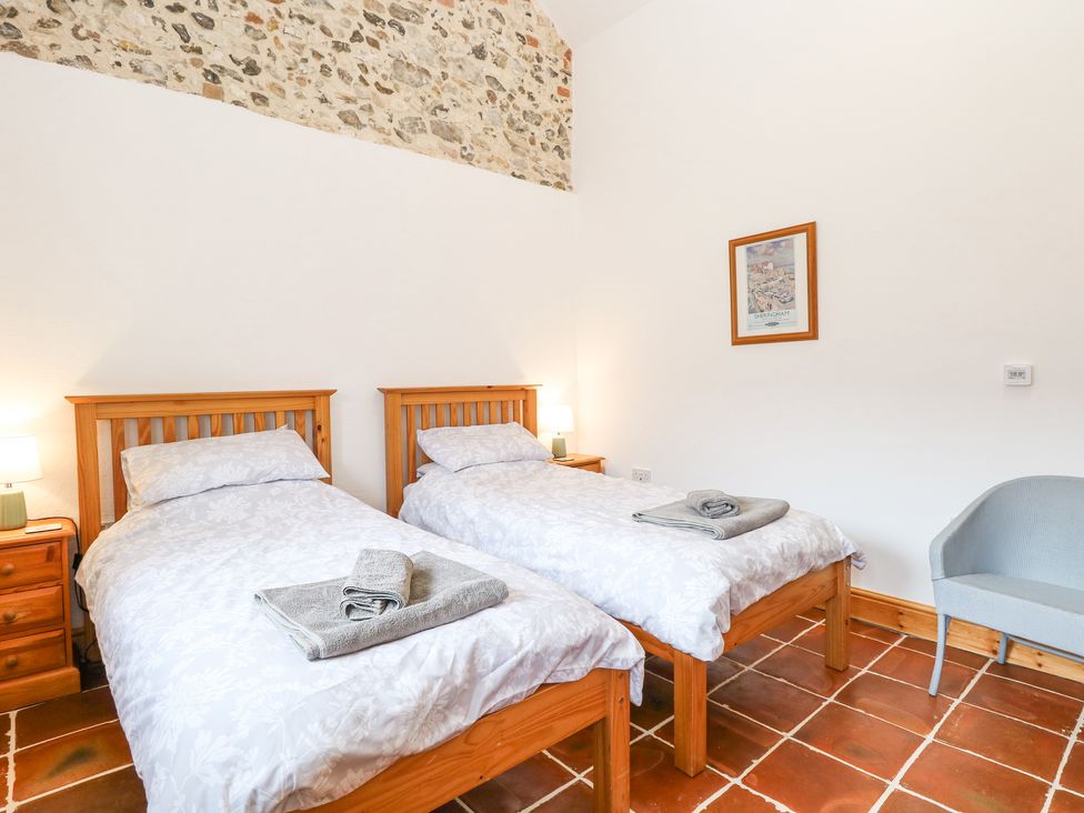 A bedroom with two single beds bedside tables with lamps framed picture and an armchair at The Old Dairy in Tittleshall near Brisley