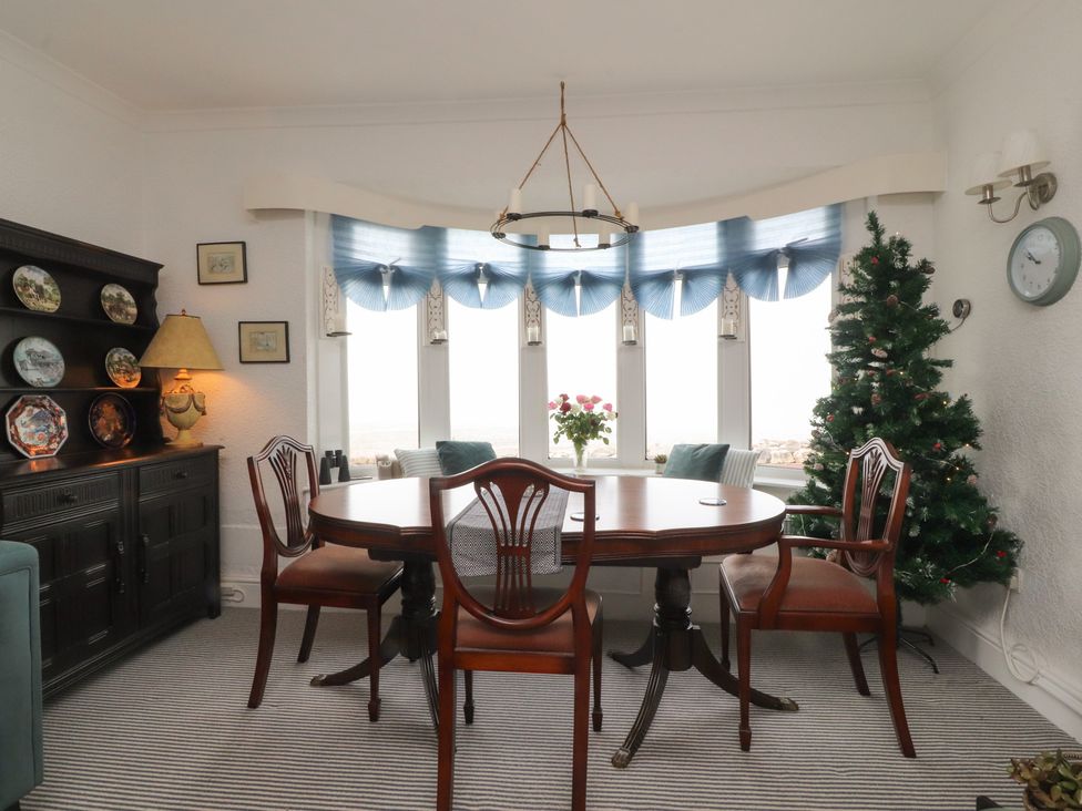 A dining room with a wooden table and chairs beside a window and a Christmas tree at Love Nest in Heysham