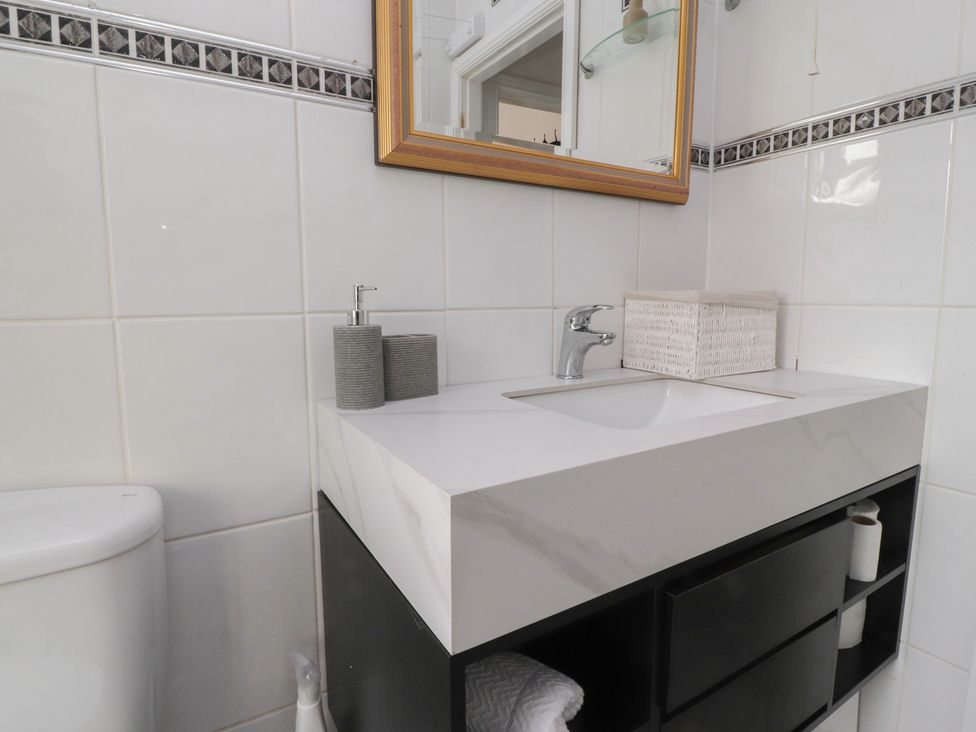 A bathroom sink with a mirror above soap dispenser and storage items near toilet at Love Nest in Heysham