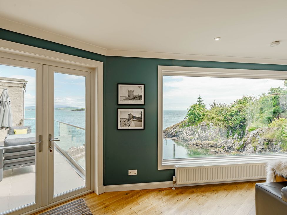 A room with large windows showing a sea view with rocky shore and plants at Balcary Tower near Palnackie