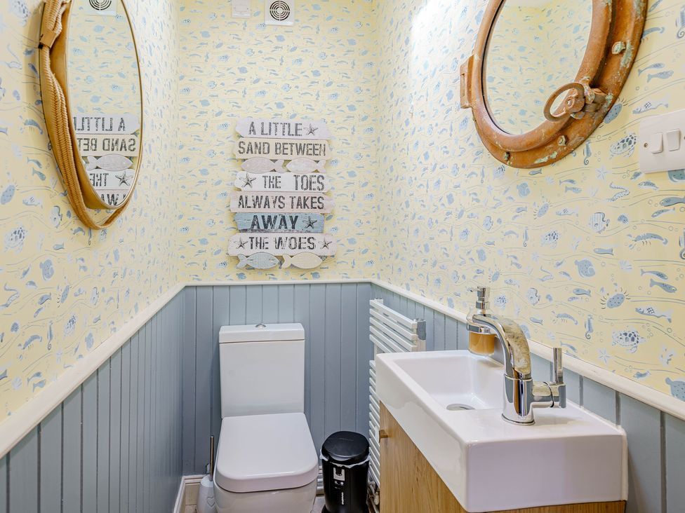 A bathroom with a toilet, sink, two round mirrors, patterned wallpaper, and a decorative sign at Balcary Tower near Palnackie