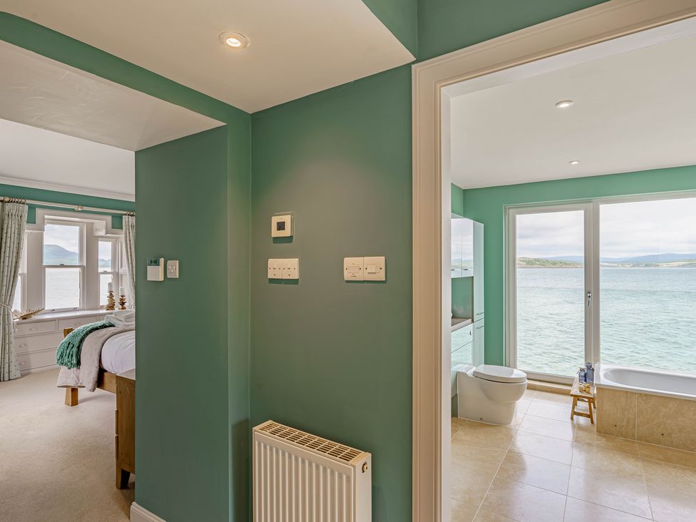 A hallway with green walls showing a bedroom with a bed and a bathroom with a toilet and bathtub with a sea view at Balcary Tower near Palnackie