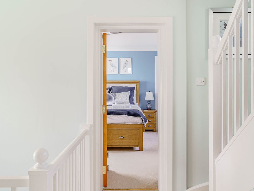 A view of a bedroom through a doorway with a wooden bed, bedside table with lamp, and blue painted wall at Balcary Tower near Palnackie