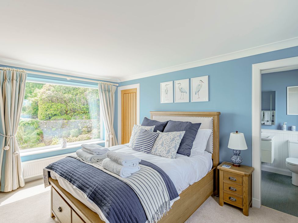 A bedroom with a bed cushions bedside table and lamp a window with curtains and an open door to a bathroom at Balcary Tower near Palnackie