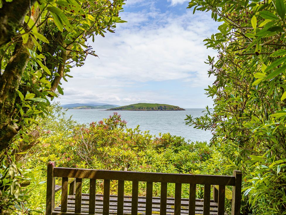 A wooden bench surrounded by greenery with a view of an island and the sea at Balcary Tower near Palnackie