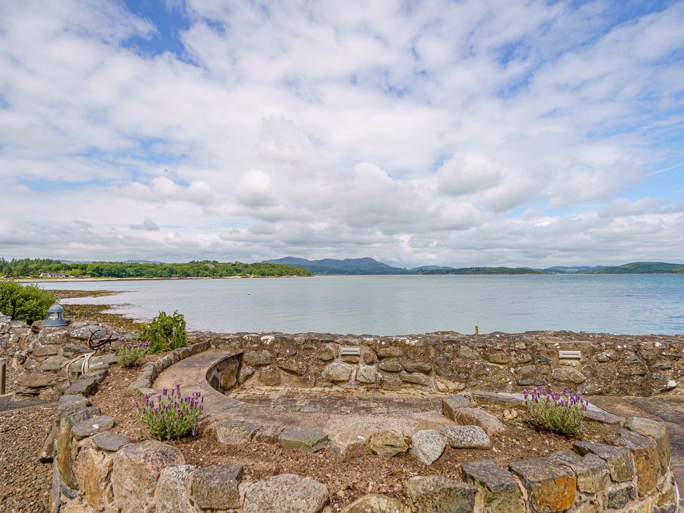 A stone wall and garden bed with purple flowers overlooking a body of water and distant hills at Balcary Tower near Palnackie