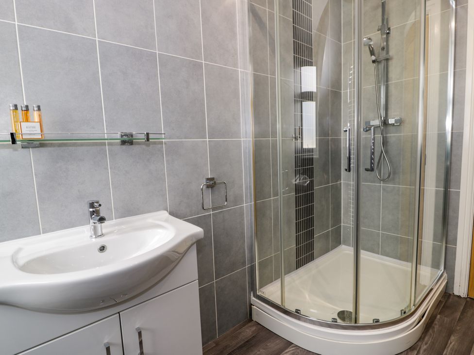 A bathroom with a white sink cabinet and a glass shower enclosure at Bwthyn Y Mor in Tal-Y-Bont
