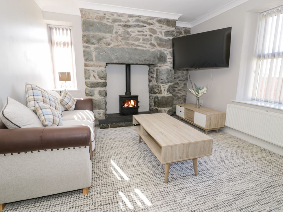 A living room with a stone fireplace a sofa a wooden coffee table TV on the wall at Bwthyn Y Mor in Tal-Y-Bont