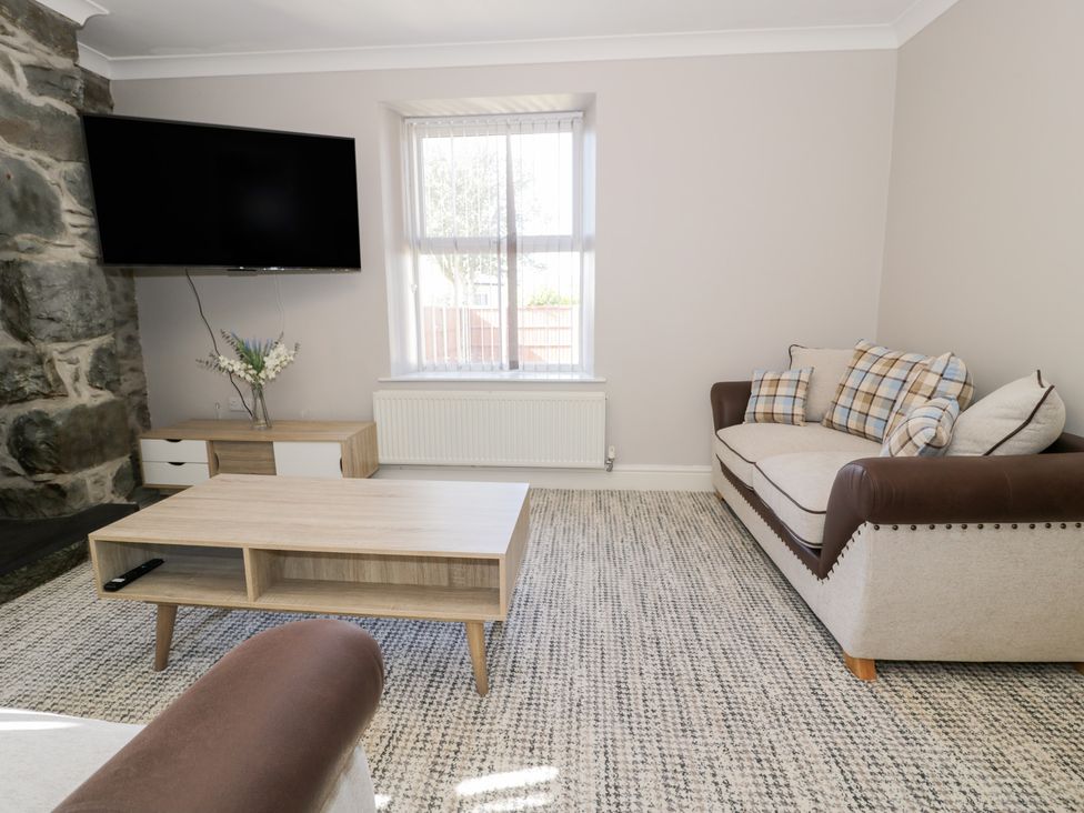A living room with a plaid cushion sofa a coffee table a wall-mounted TV and a sideboard with flowers at Bwthyn Y Mor in Tal-Y-Bont