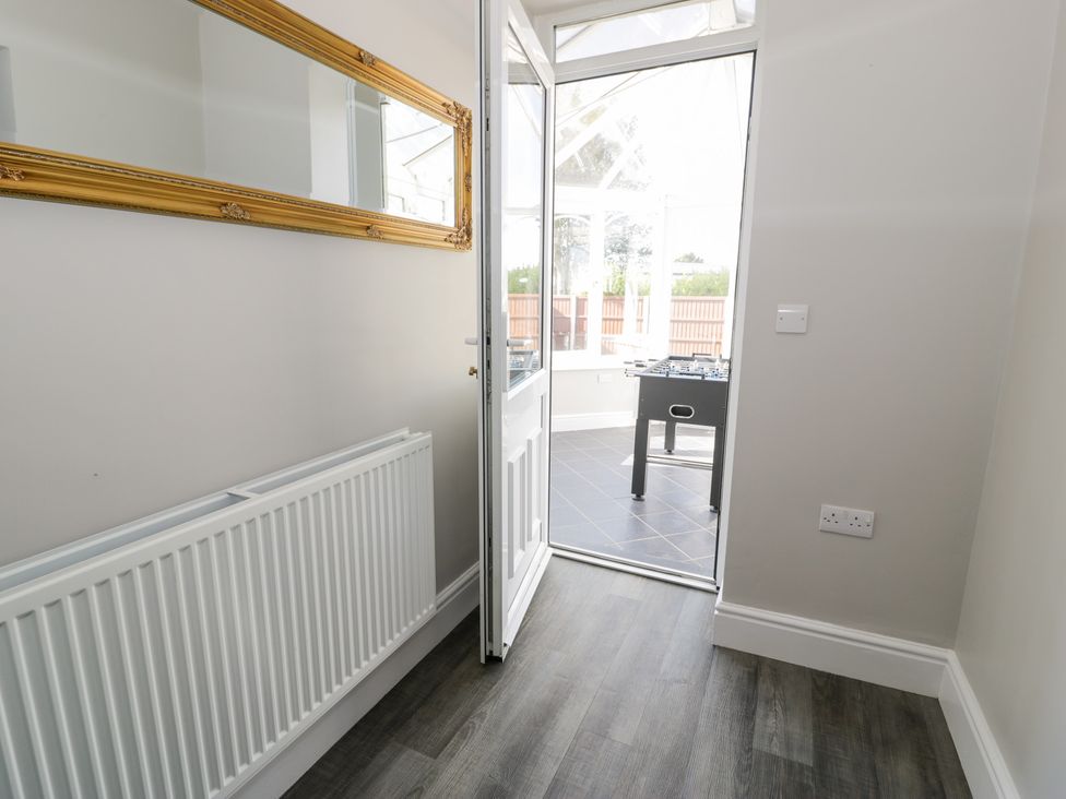 A hallway with a radiator and a large framed mirror leading to a room with a foosball table at Bwthyn Y Mor in Tal-Y-Bont