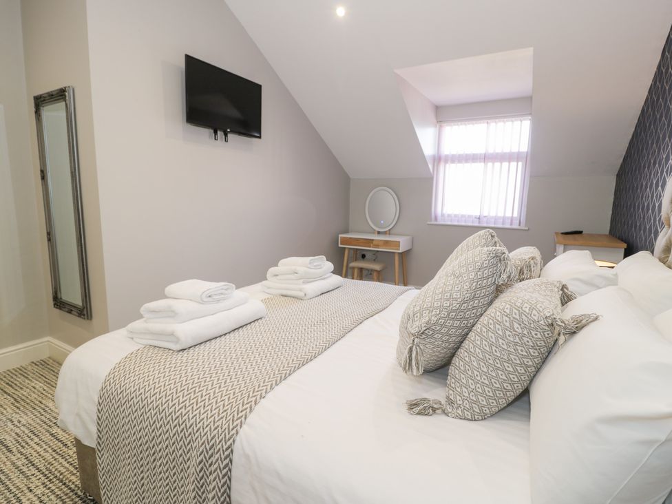 A bedroom with a bed with folded towels pillows a wall-mounted TV a mirror and a small desk at Bwthyn Y Mor in Tal-Y-Bont