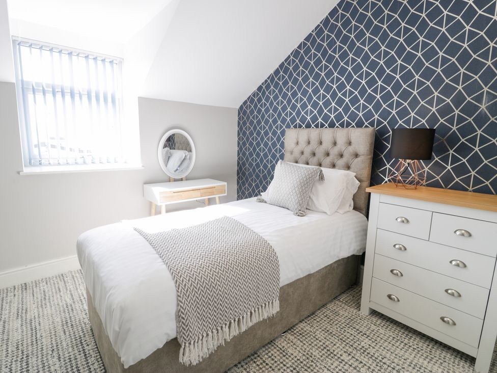 A bedroom with a single bed a bedside table with a lamp a wooden dresser and a vanity table with a round mirror at Bwthyn Y Mor in Tal-Y-Bont