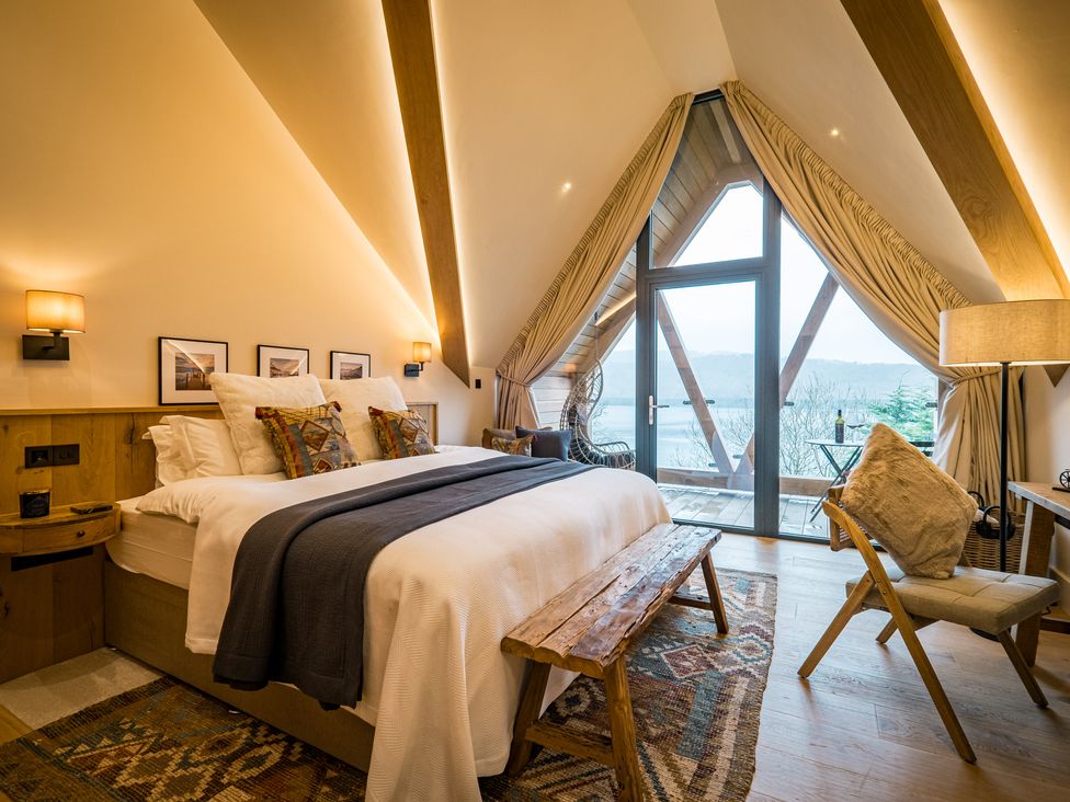A bedroom with a large bed wooden bench chair lamp and glass doors leading to a balcony at The Ridge in Bowness-On-Windermere
