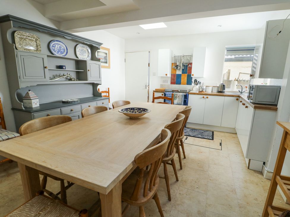 A kitchen with a wooden dining table and chairs a gray cabinet with plates and a white cabinetry with appliances at The Harbour in Rhosneigr