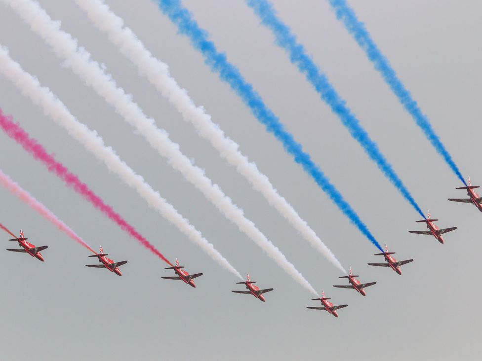 Red airplanes flying in formation with red white and blue smoke trails in the sky