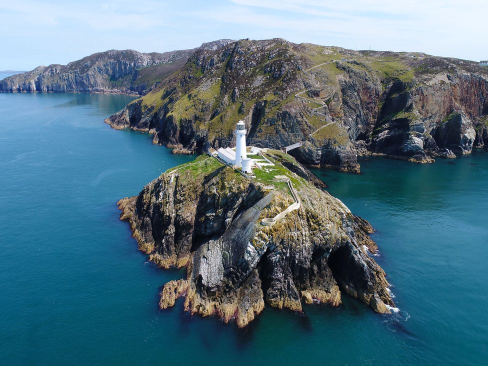 A lighthouse on a rocky promontory surrounded by water and cliffs at The Harbour in Rhosneigr