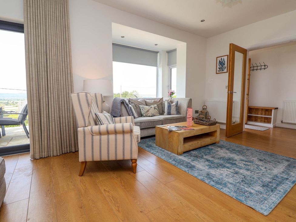 A living room with a striped armchair a sofa with cushions a wooden coffee table and a blue rug at Buzzards View in Dyserth