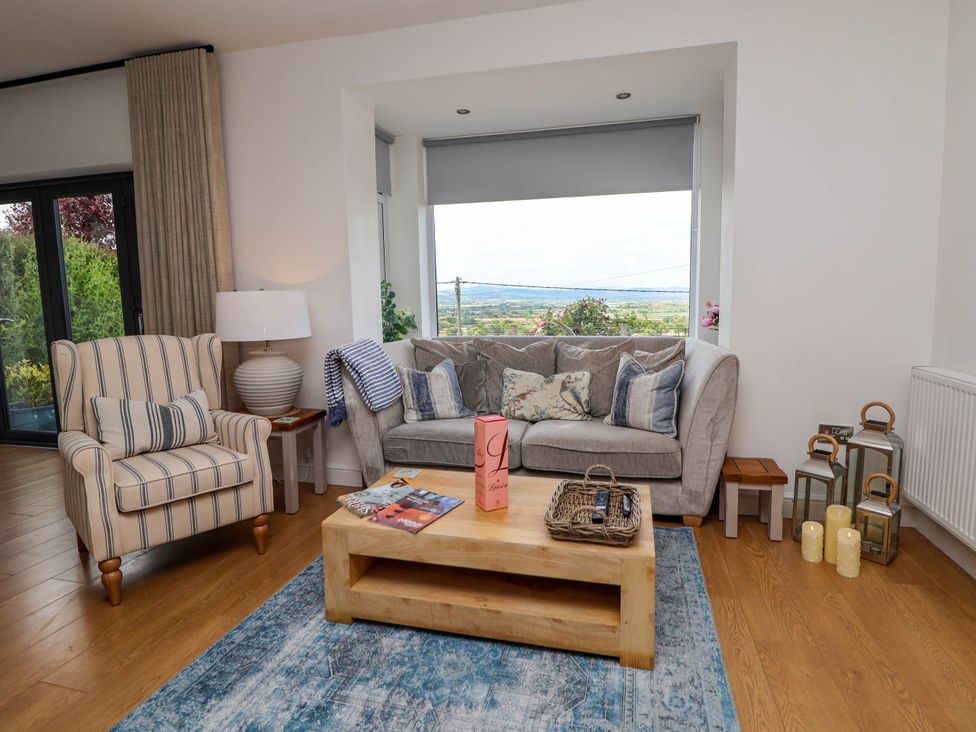 A living room with a sofa and armchair a wooden coffee table and large window at Buzzards View in Dyserth