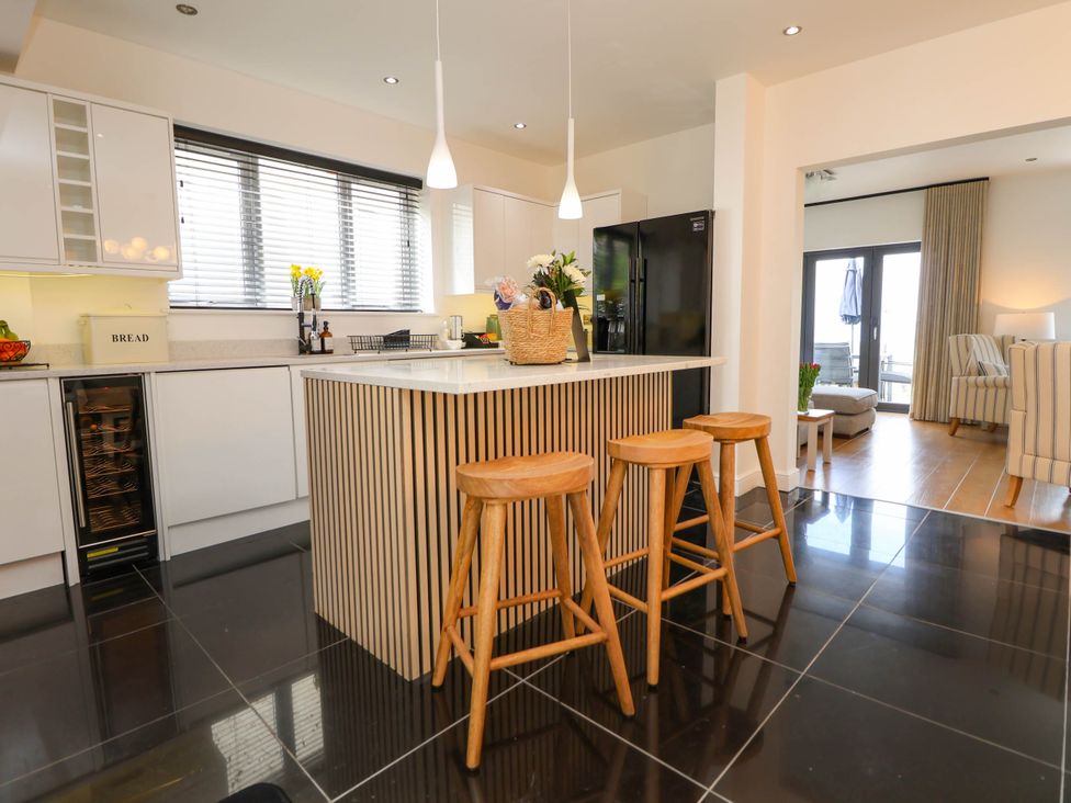 A kitchen with a central island and three wooden stools with a living room visible through an open doorway at Buzzards View in Dyserth