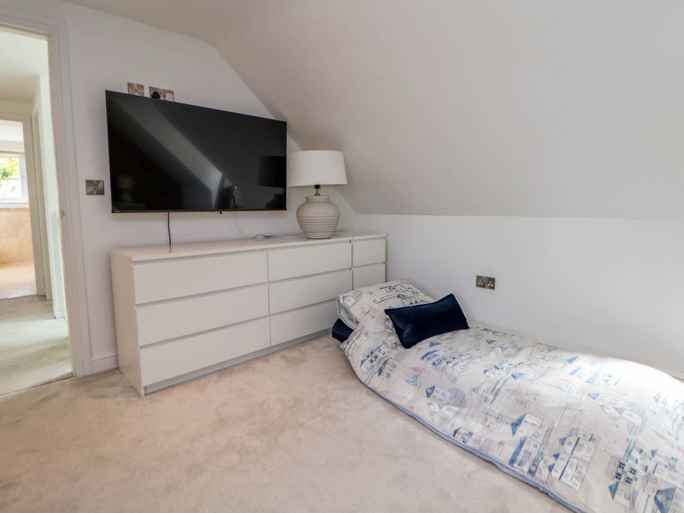 A bedroom with a low bed near a white dresser with a lamp and a wall mounted television at Buzzards View in Dyserth