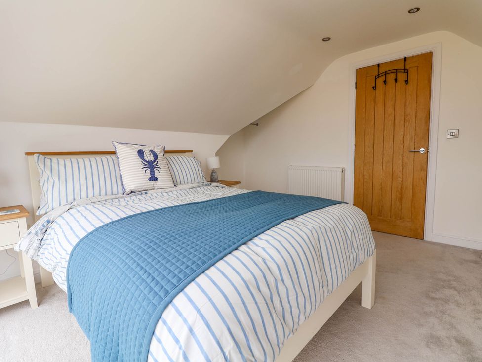A bedroom with a bed with blue and white striped bedding and a wooden door at Buzzards View in Dyserth