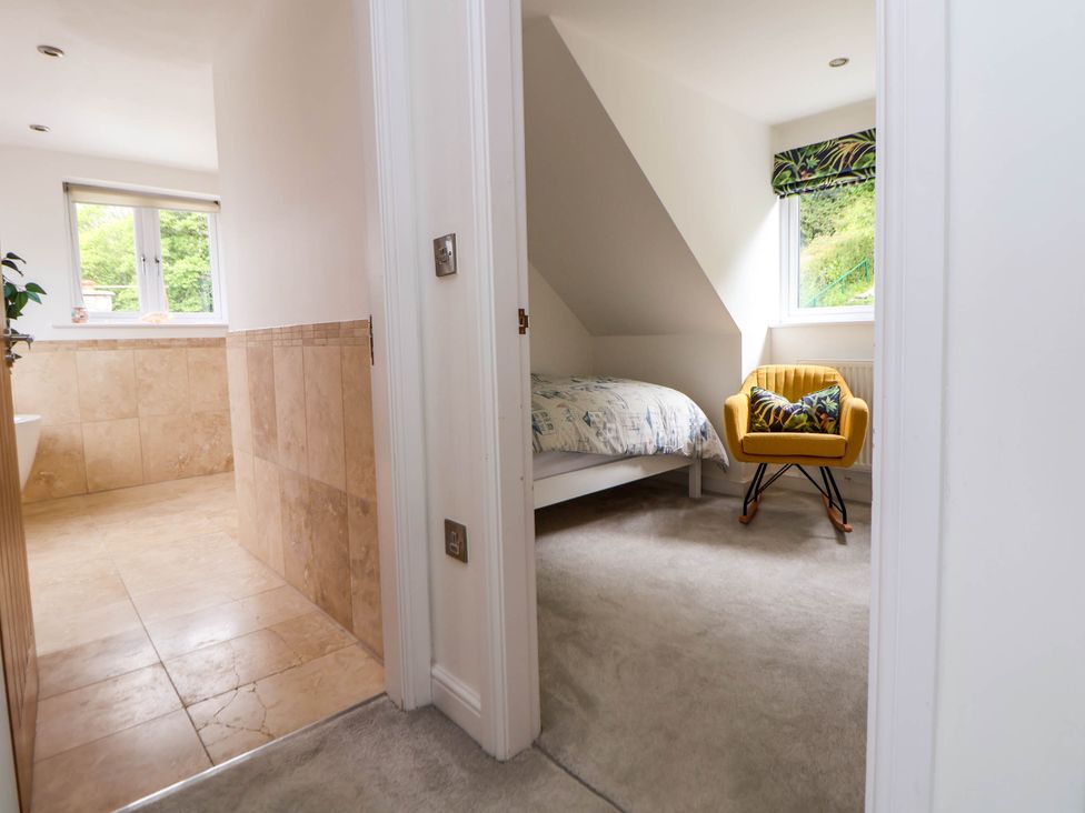 A bathroom with tiled floor and walls and a bedroom with a bed and a yellow chair at Buzzards View in Dyserth