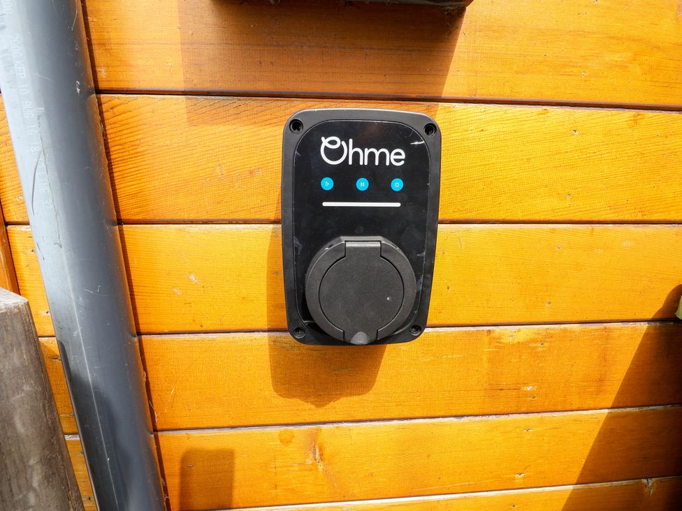 A black Ohme electric vehicle charger mounted on a wooden wall with a grey pipe running beside it at Buzzards View in Dyserth