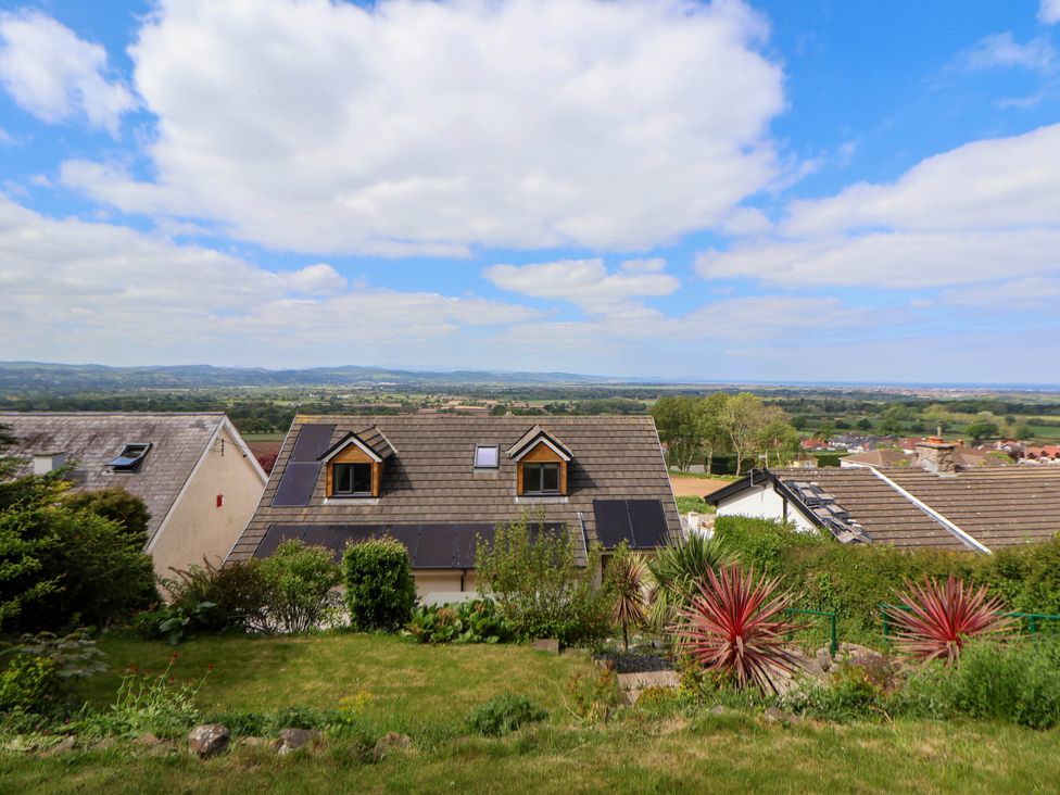 A garden with grass and plants overlooking rooftops with solar panels and a distant landscape at Buzzards View in Dyserth